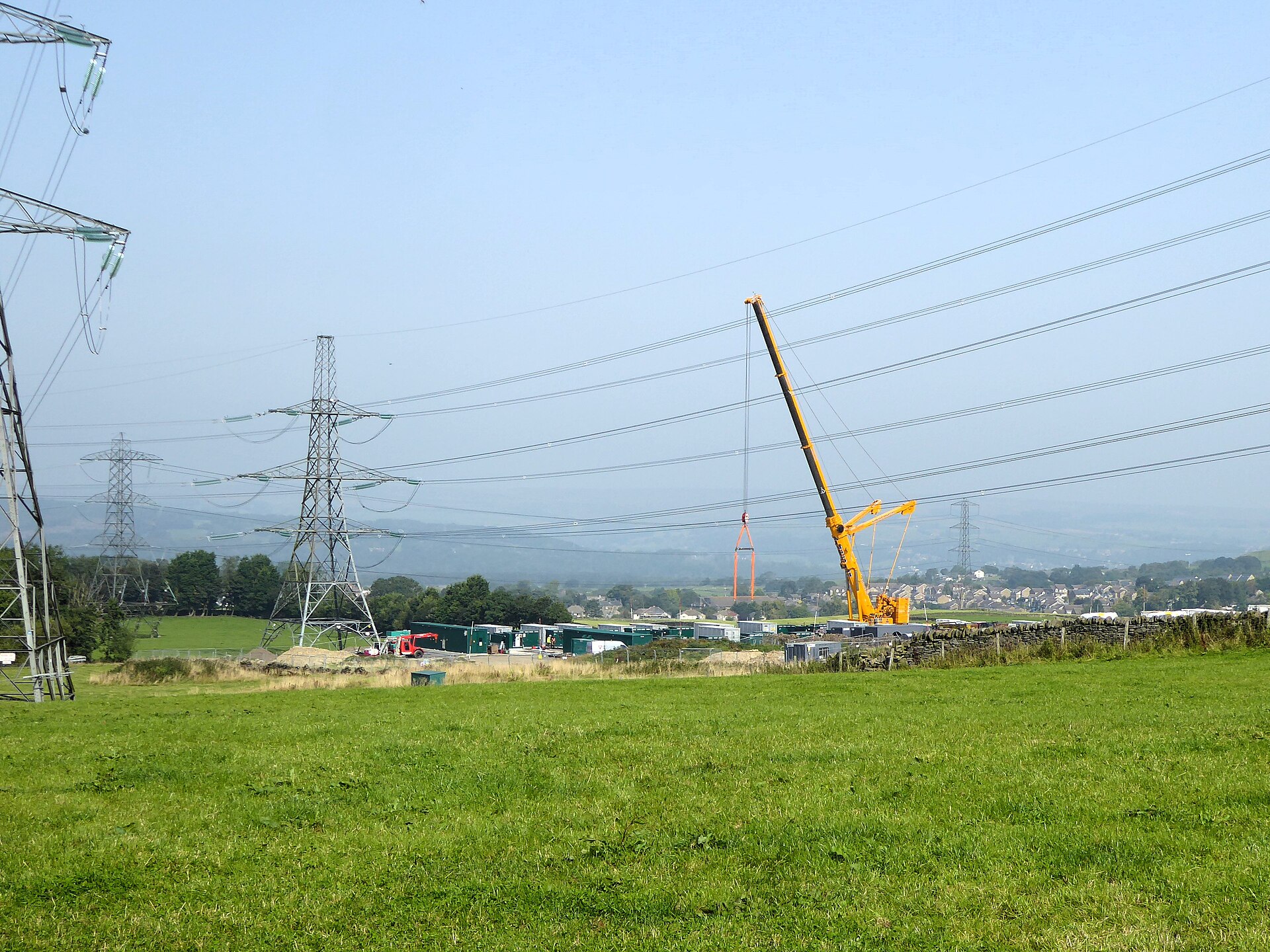 A crane working at a construction site, with electricity pylons in the background